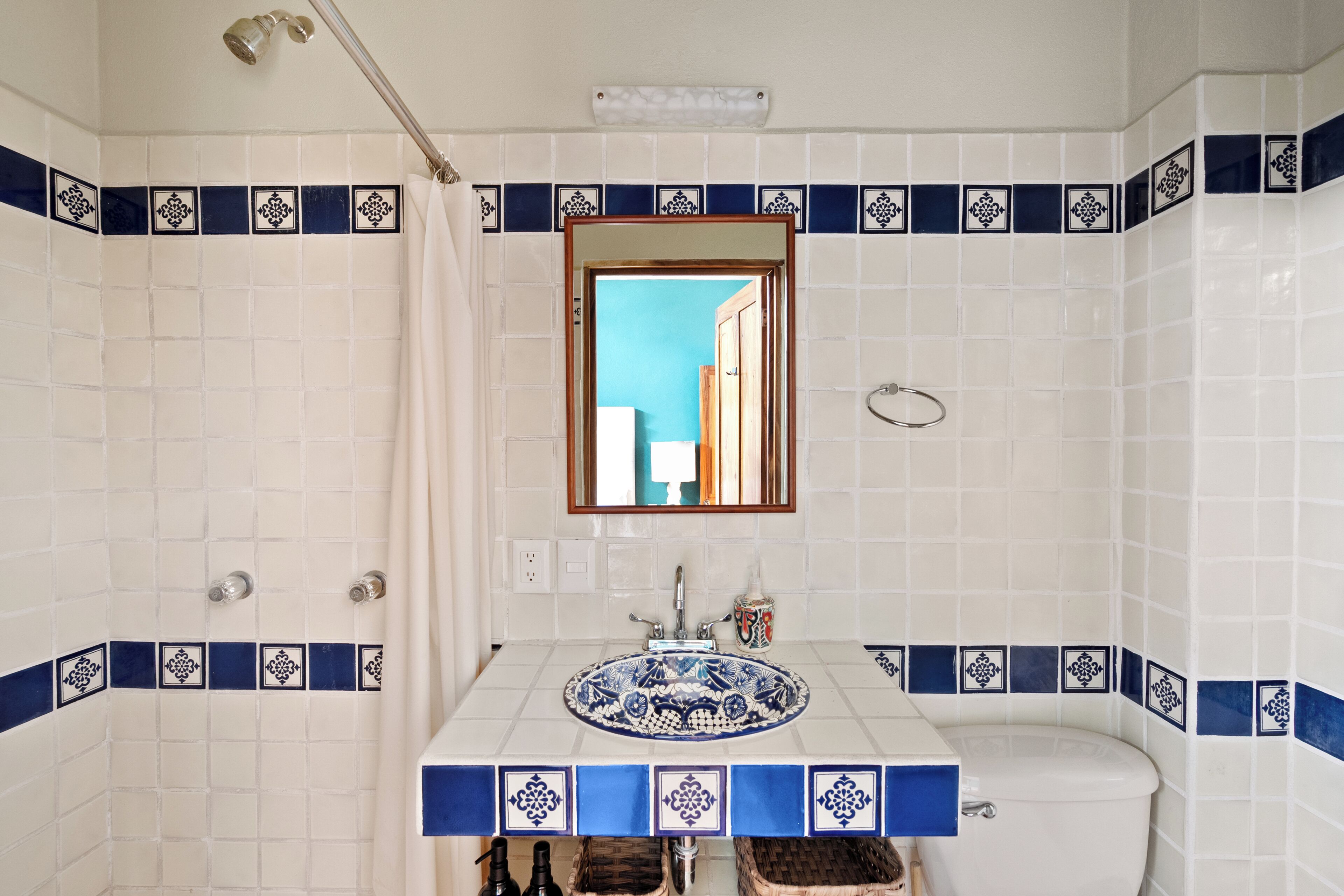 A bathroom with a white sink, blue decorative tiles, a mirror, and a shower.