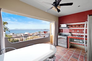 Ein Balkon mit Blick auf den Ozean und die Stadtlandschaft, eine Küche mit roten und weißen Fliesen und ein Essbereich mit Tisch und Stühlen.