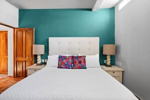 Ein Schlafzimmer mit einem weißen Bett, teal-farbenen Wänden, einer Holztür und zwei Nachttischlampen.