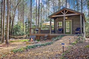 Uma cabana com varanda, área de estar externa, lareira e vista para a floresta.