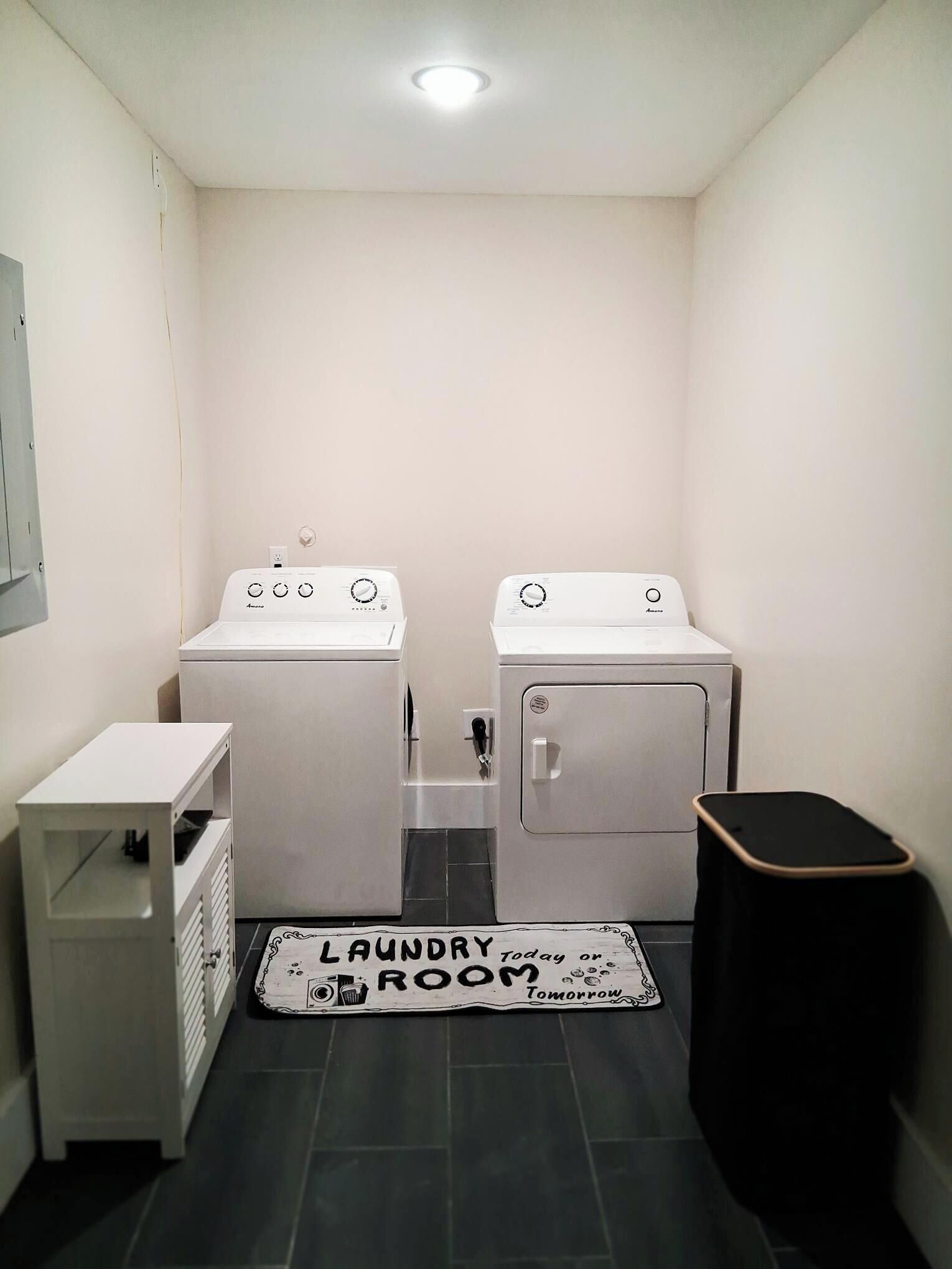 A laundry room with two washing machines, a drying rack, and a trash bin.