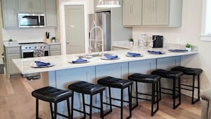 Una cocina moderna con una isla central, taburetes de bar y un refrigerador de acero inoxidable.