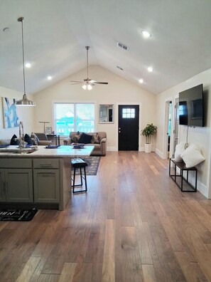 A spacious living area with a high ceiling, a ceiling fan, a large window, a black door, and a flat-screen TV mounted on the wall. - Bright & Airy Upstairs 3BR/2BA Oasis Near Downtown (Tulsa)