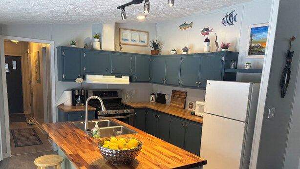 Una cocina moderna con una isla de madera, taburetes de bar, un fregadero y un refrigerador.