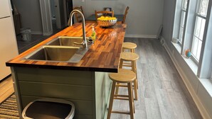 Una cocina con una isla de madera, pileta de acero inoxidable y taburetes de madera.