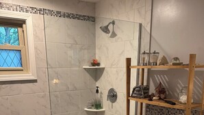 Un bagno con doccia, toilette, mensole con articoli da toilette e una finestra con vista.