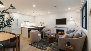 A modern living room with a fireplace, a dining area, and a kitchen. - Monashee Meadows (Revelstoke)