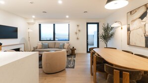 A modern living room with a sofa, a dining table, and a large window with a view. - Monashee Meadows (Revelstoke)