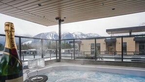 A hot tub with a view of snow-capped mountains, a bottle of champagne, and a glass on a balcony. - Monashee Meadows (Revelstoke)