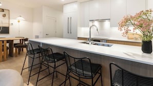 A modern kitchen with white cabinets, a stainless steel sink, and a bar area with black chairs. - Monashee Meadows (Revelstoke)