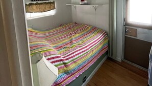 Una habitación pequeña con cama individual, un edredón de rayas coloridas, un cuadro en la pared y una ventana con vistas al exterior.
