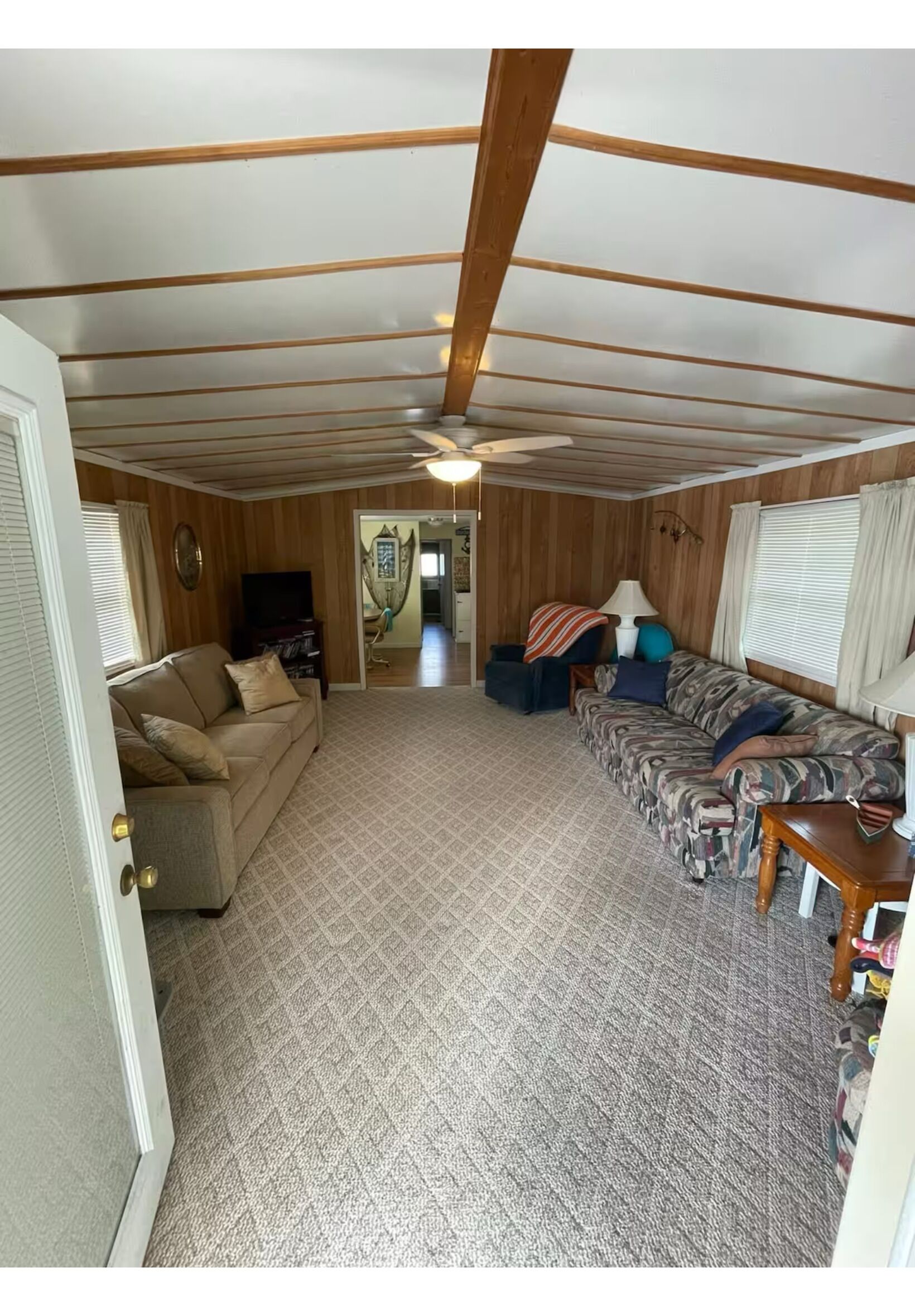 A cozy RV interior with a patterned carpet, wooden ceiling beams, a sofa, a chair, and a table.