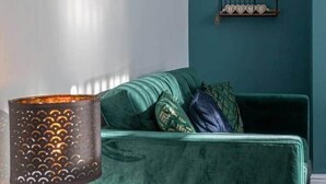 Een kamer in teal met een groene fluweelzitzak, een klein rond tafeltje met een lamp en twee ingelijste foto’s aan de muur.