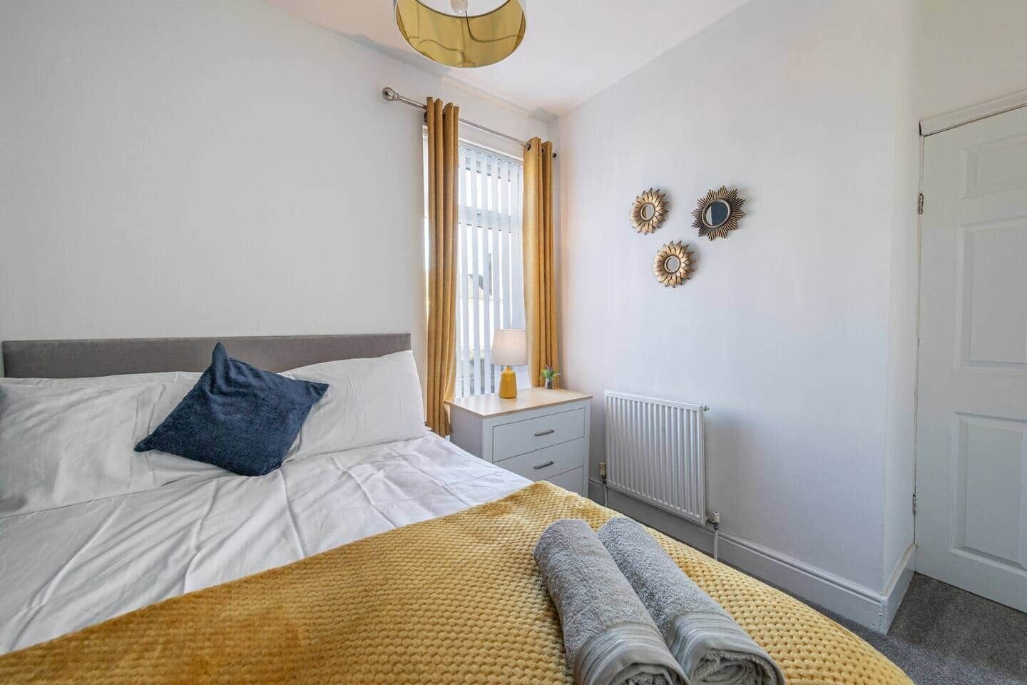A bedroom with a bed, a bedside table, a lamp, and a window with curtains.