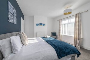 Un dormitorio con cama, mesita de noche, radiador, ventana con cortinas y decoración en la pared.