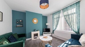 Een woonkamer met teal muren, een groene bank, een blauwe bank, een kleine witte schoorsteen, een ronde tafel en een televisie.