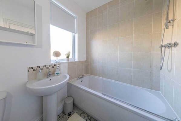 Un baño con un lavamanos blanco, una bañera y una ducha. Hay una ventana sobre el lavamanos y un espejo en la pared.