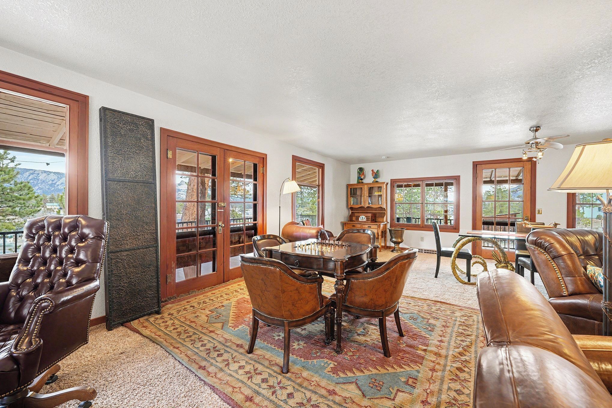 A spacious living room with a large wooden dining table surrounded by leather chairs, a leather sofa, and a patterned rug.