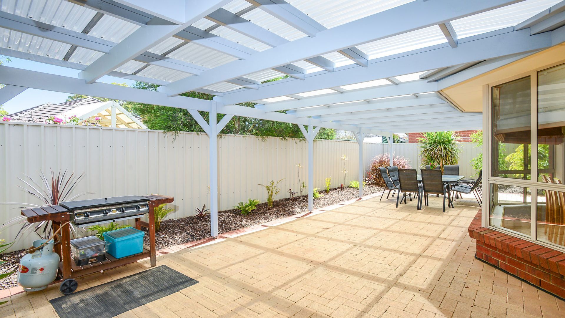 A covered patio with a grill, seating area, and a view of the backyard.