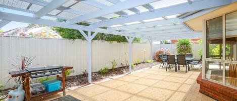 A covered patio with a grill, seating area, and a view of the backyard.