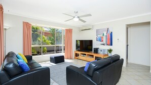 A living room with a flat-screen TV, two black leather sofas, a wooden coffee table, and a large window with curtains. - 2 Marto Court, Normanville (Normanville)