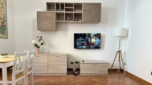 A modern living room with a wooden cabinet, a TV mounted on the wall, a glass coffee table, and a floor lamp. - PAOLINA HOME IN ROME (Roma)