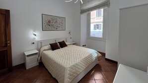 A bedroom with a bed, bedside tables, a wall-mounted light fixture, a window with blinds, and a framed picture on the wall. - PAOLINA HOME IN ROME (Roma)