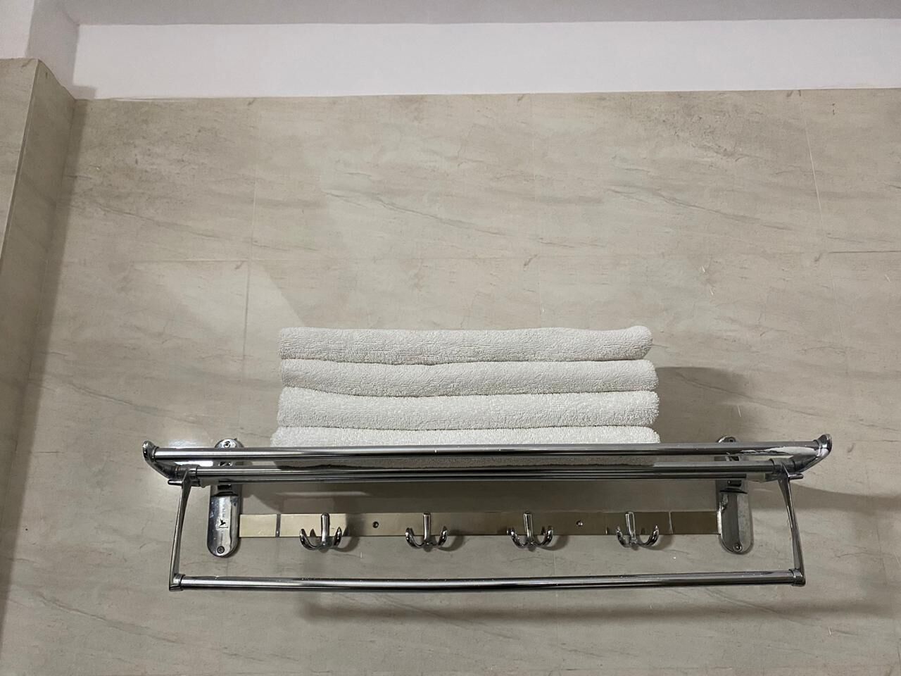 A metal towel rack with multiple hooks against a tiled wall.