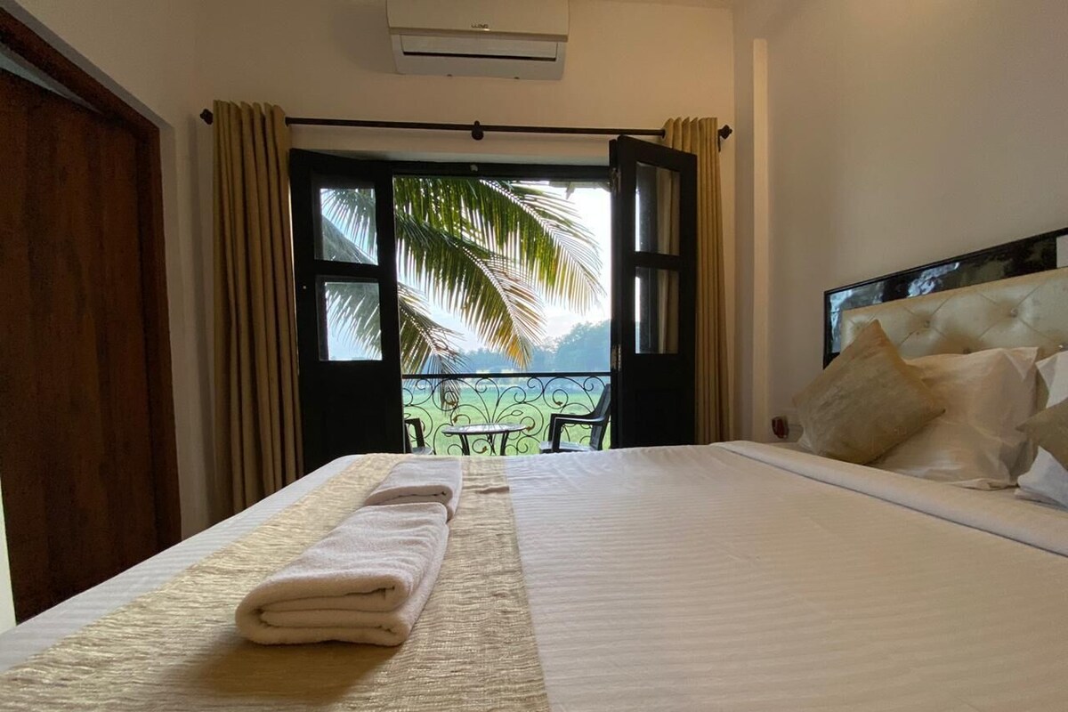 Quarto de hotel com cama, varanda e vista para palmeiras, além de ar condicionado.