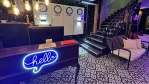 A hotel reception area with a neon 'hello' sign, clocks displaying times in Istanbul, Paris, Dubai, and New York, and a staircase leading to upper floors. - The Little Prince Hotel (Istanbul)