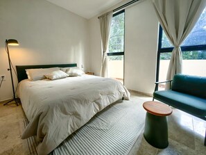 Ein Schlafzimmer mit einem Bett, einem grünen Sofa, einer Stehlampe und Blick ins Freie durch ein Fenster.