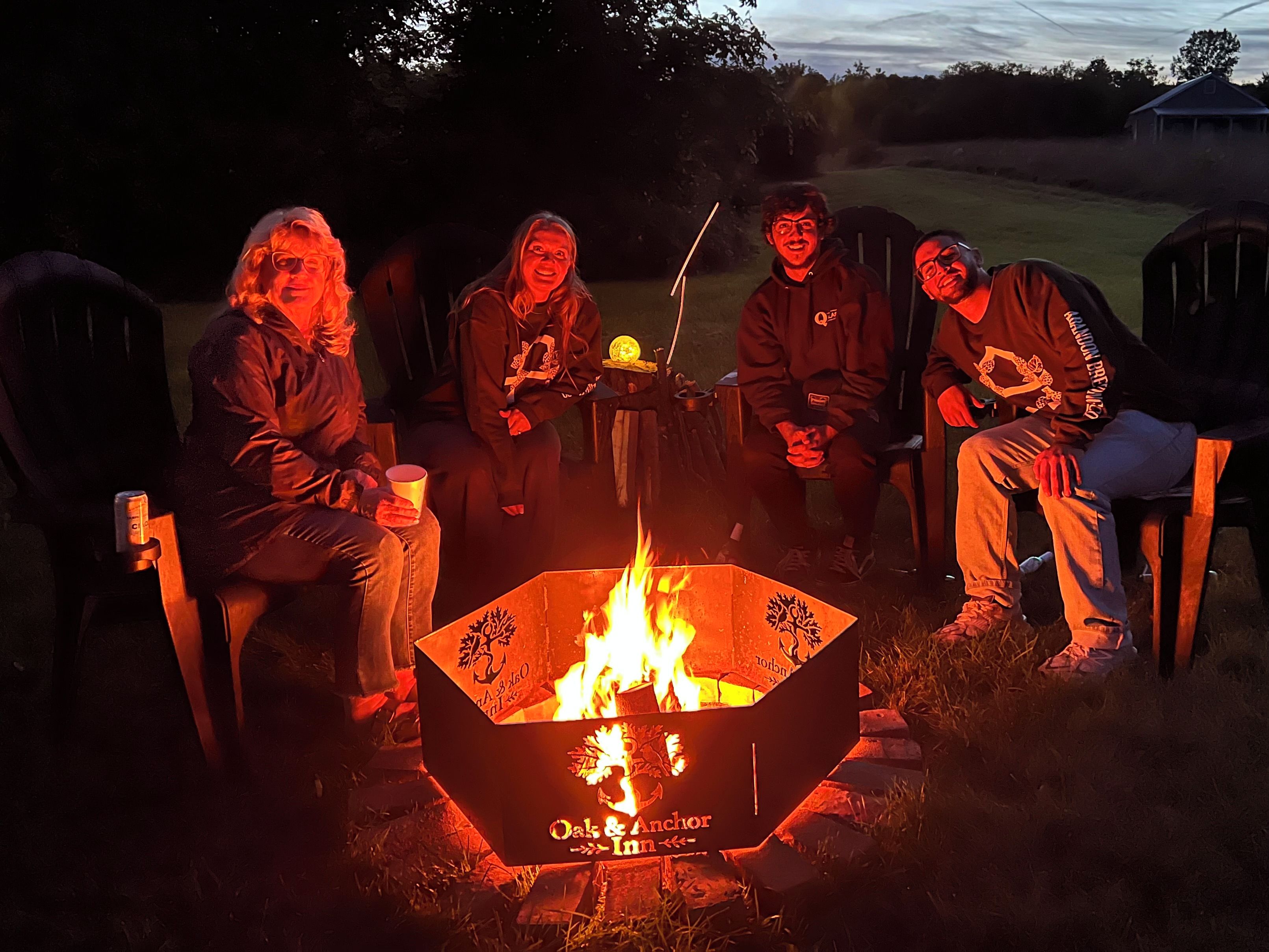 Four individuals seated around a campfire in an outdoor setting.