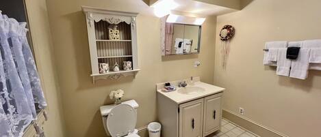 A bathroom with a toilet, sink, vanity, mirror, towel rack, and decorative items.