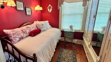 Une chambre à coucher avec un lit en bois, une table de chevet, une fenêtre avec des stores et une petite table sur laquelle se trouve une théière.