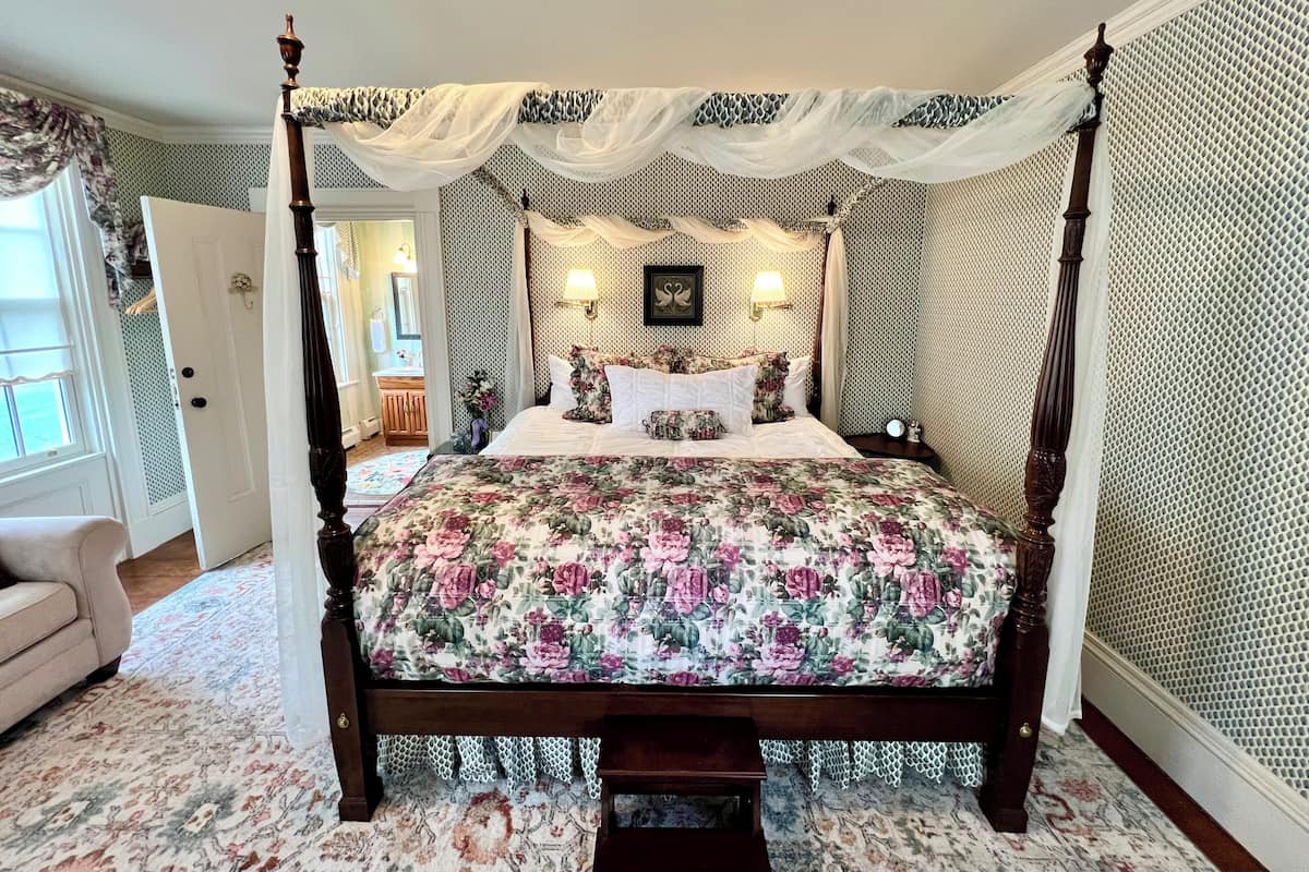 Uma cama de dossel com roupa de cama florida, um toldo e arandelas.