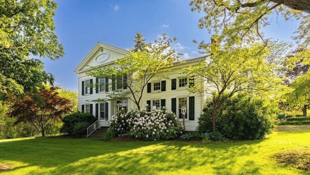 A large, two-story house with a prominent front porch, surrounded by lush greenery and a well-maintained lawn.