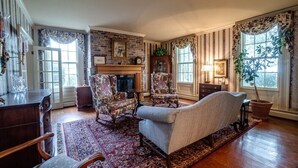 A traditional living room with a fireplace, floral armchairs, a sofa, and a large window with curtains.