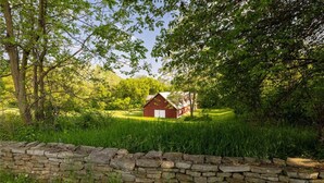 A rustic barn surrounded by lush greenery and a stone wall.