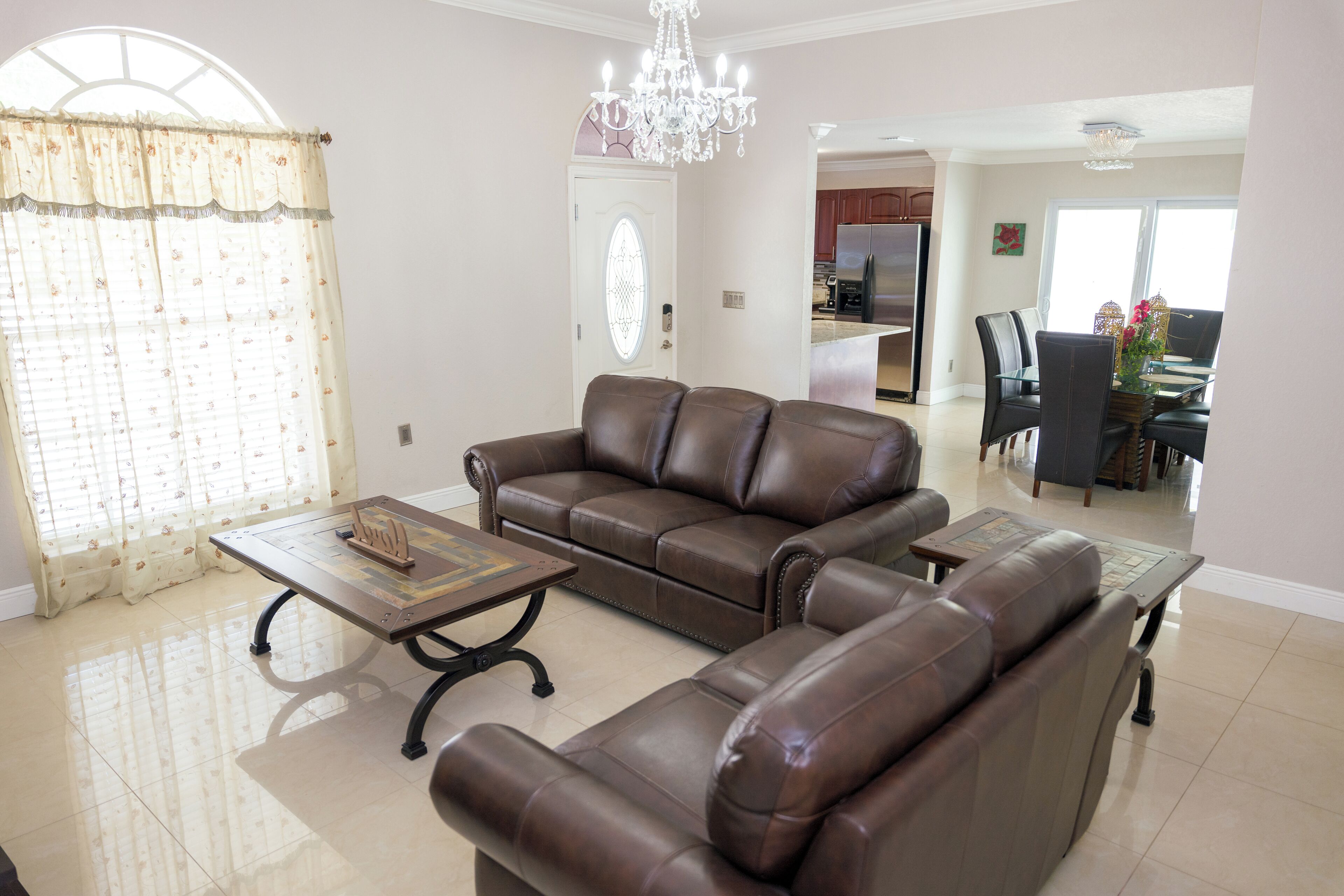 A living room with a brown leather sofa, a coffee table, and a chandelier.