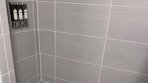 Une salle de bain moderne avec une baignoire blanche, des carreaux gris et un distributeur de savon fixé au mur.