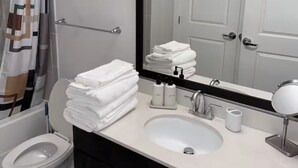 Une salle de bain avec des toilettes, un lavabo et un miroir. Des serviettes sont pliées sur le comptoir et il y a un rideau de douche.