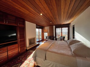 A bedroom with a large bed, wooden ceiling, built-in TV, and a fireplace. - Hortênsia Boutique - Private Chalet 2 (Campos do Jordão)