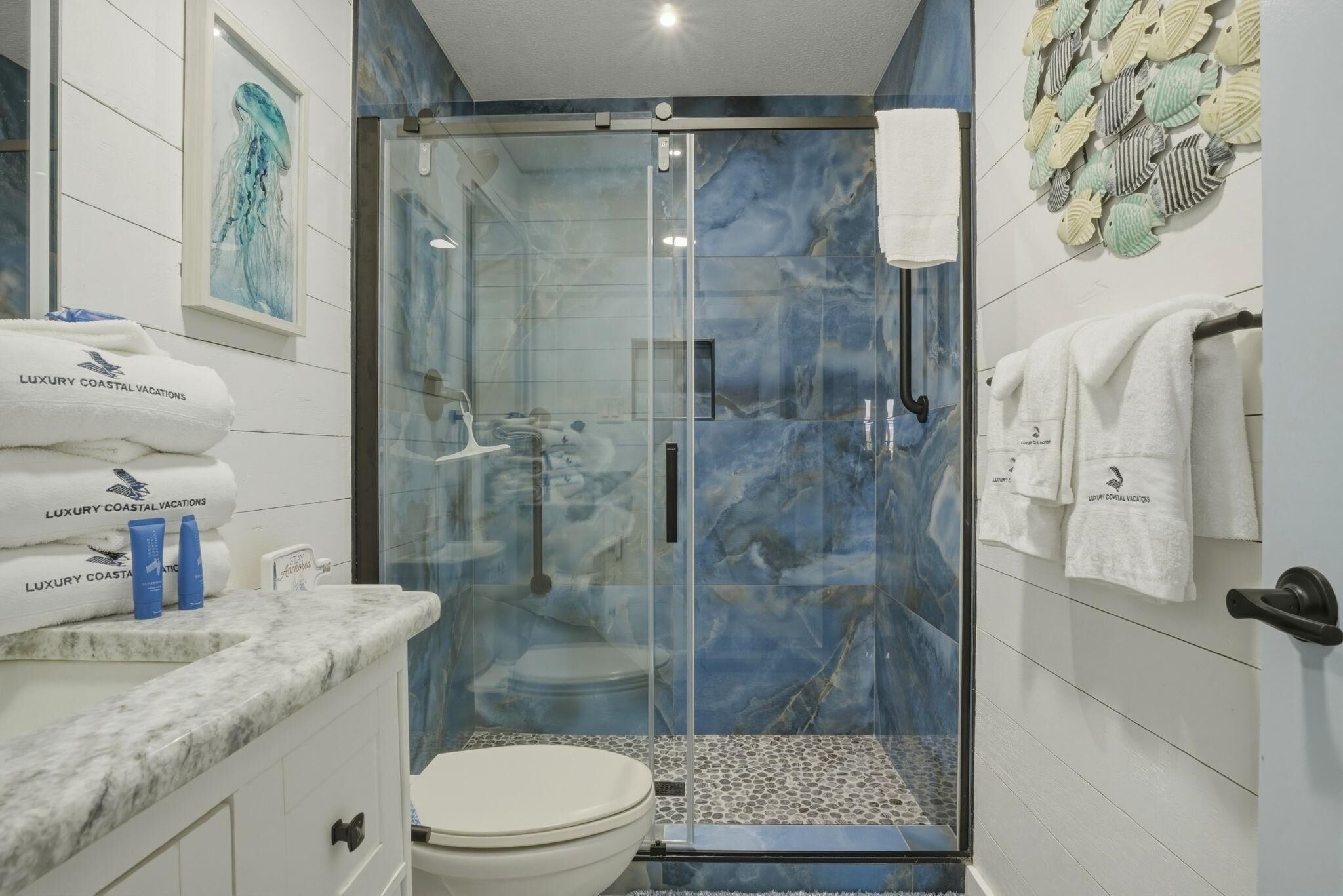 A bathroom with a glass-enclosed shower, a marble countertop, and a toilet.