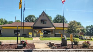 Un bâtiment doté d’un toit triangulaire et d’une façade jaune et grise. Deux drapeaux flottent sur des mâts situés devant le bâtiment.