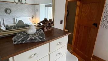 A bedroom with a large mirror, a dresser with drawers, a white chair, and a wooden door.