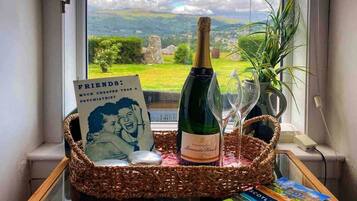 Una bottiglia di champagne, un bicchiere, un libro e una foto incorniciata su un tavolo vicino a una finestra con vista su un paesaggio.