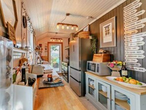 Une cuisine avec des meubles de rangement en bois, un réfrigérateur, un four à micro-ondes et un panier de fruits posé sur le comptoir.