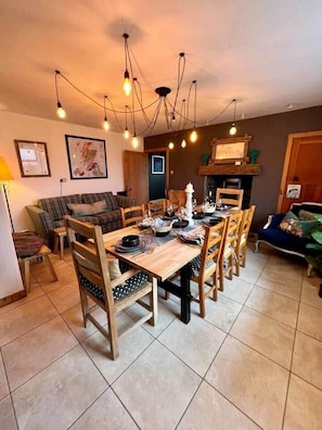 Un comedor con una mesa y sillas de madera, una araña y un sofá al fondo.