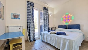 Een slaapkamer met een bed, een bureau en een stoel. Er is een raam met gordijnen en een wandlamp.