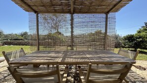 Een overdekte eethoek buiten, met een tafel en stoelen, omgeven door een gaashek.